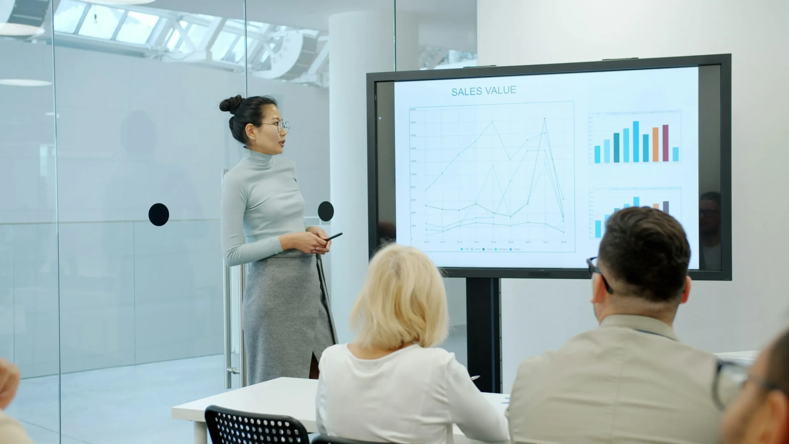 Marketing professional presenting strategy slides to executive team in a modern conference room with data visualizations on screen